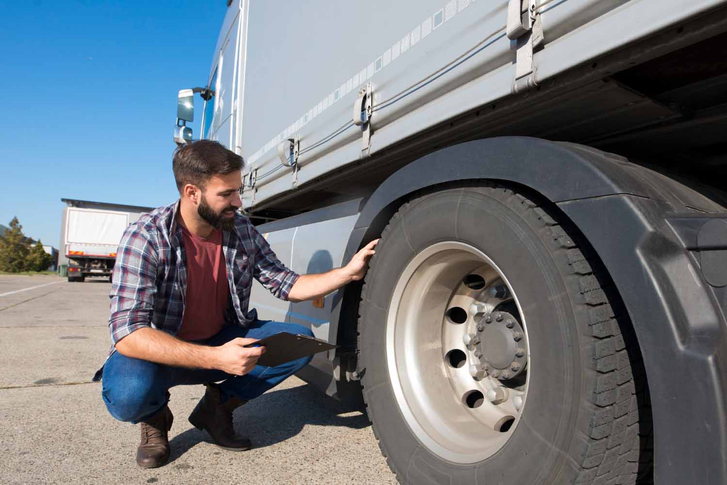 A man squating next to a semi truck inspecting one of the tires.